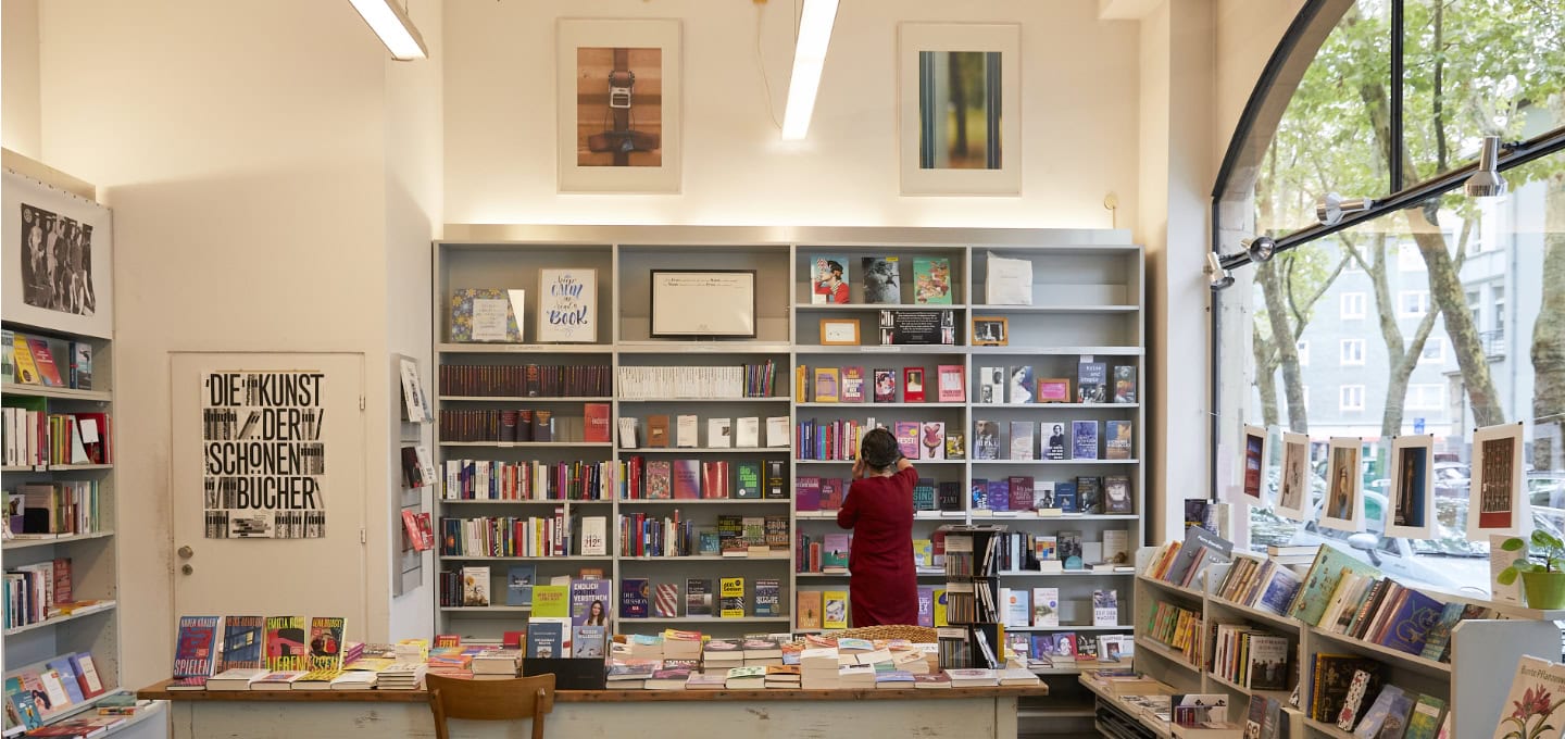 Person stöbert in den Bücherregalen eines gemütlichen Buchladens in Köln